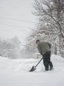 Man shoveling snow after a winter storm. Surebuild Restoration can assist with winter storm damage restoration and repairs